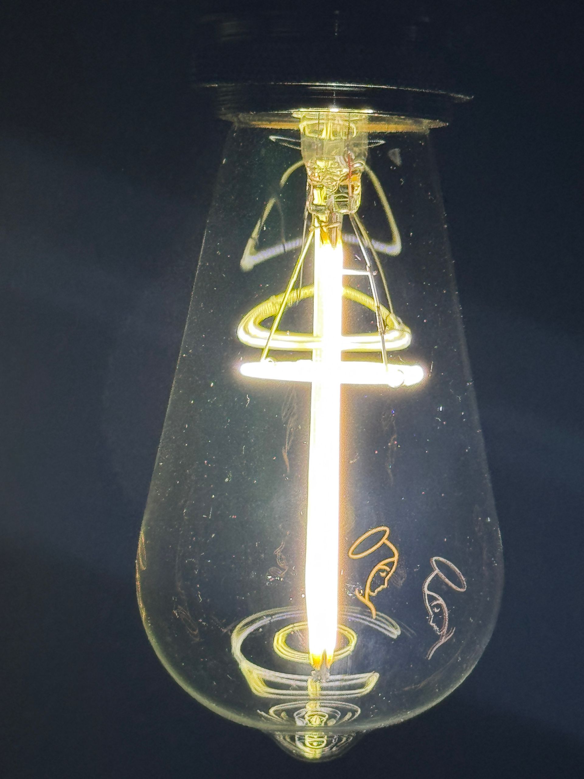 Lightbulb with glowing filament; drawings of angels inside the glass.