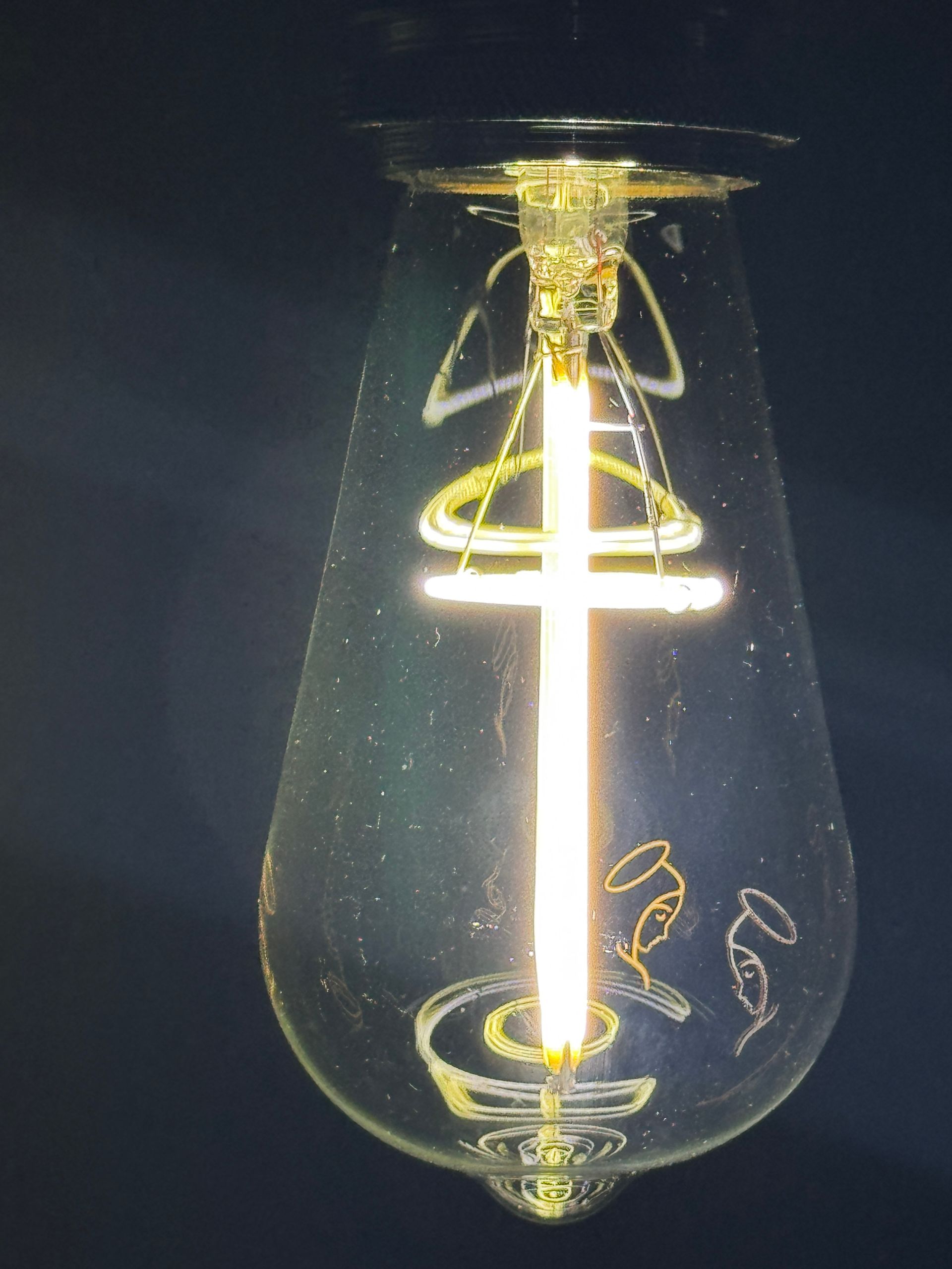 Lightbulb with a glowing cross and angel figures, in a dark setting.