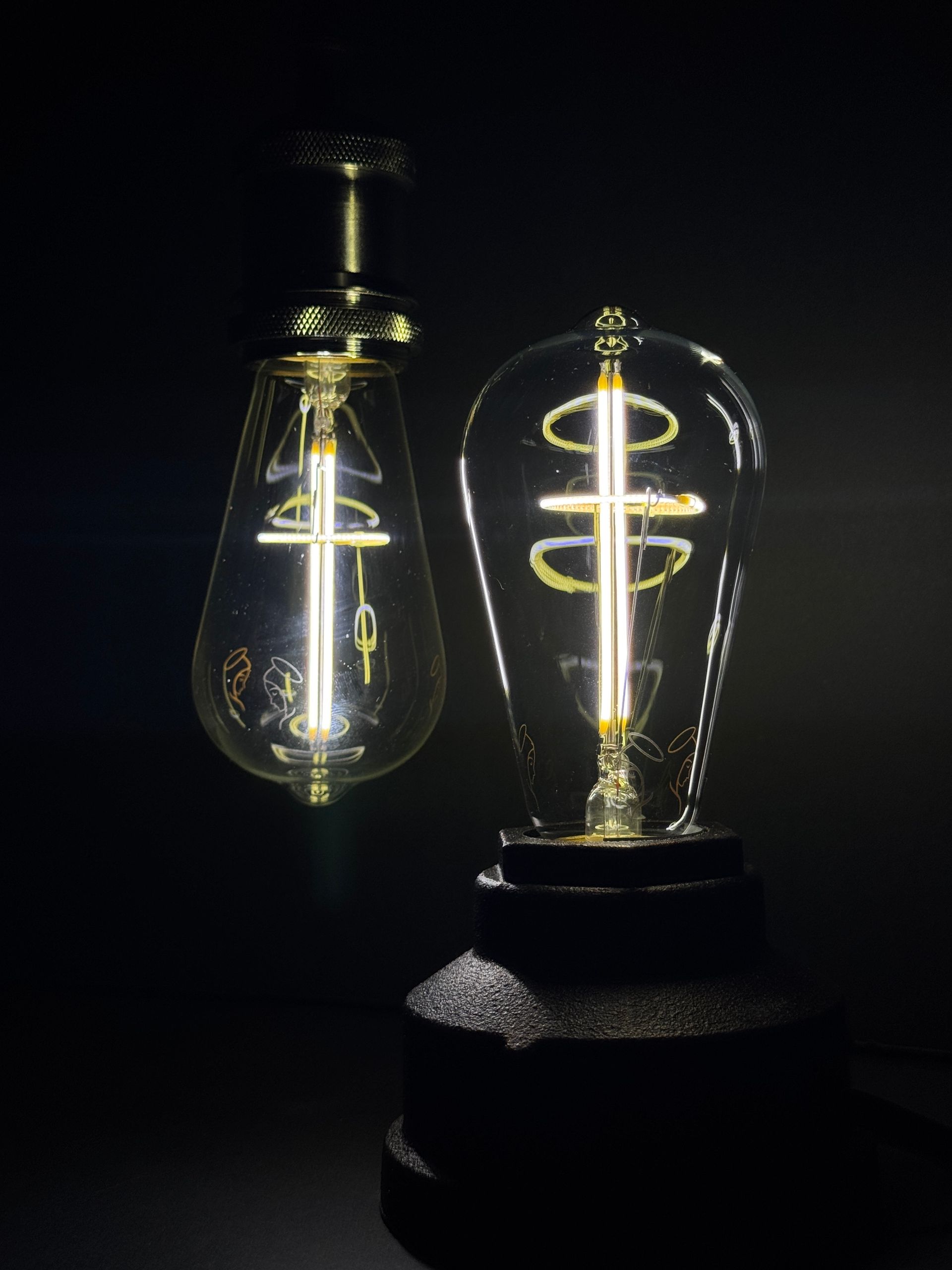 Two glowing Edison light bulbs with visible filaments against a dark background.