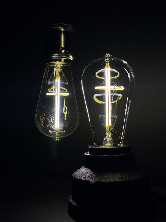 Two glowing Edison-style light bulbs, one suspended, the other on a dark base, against a black background.