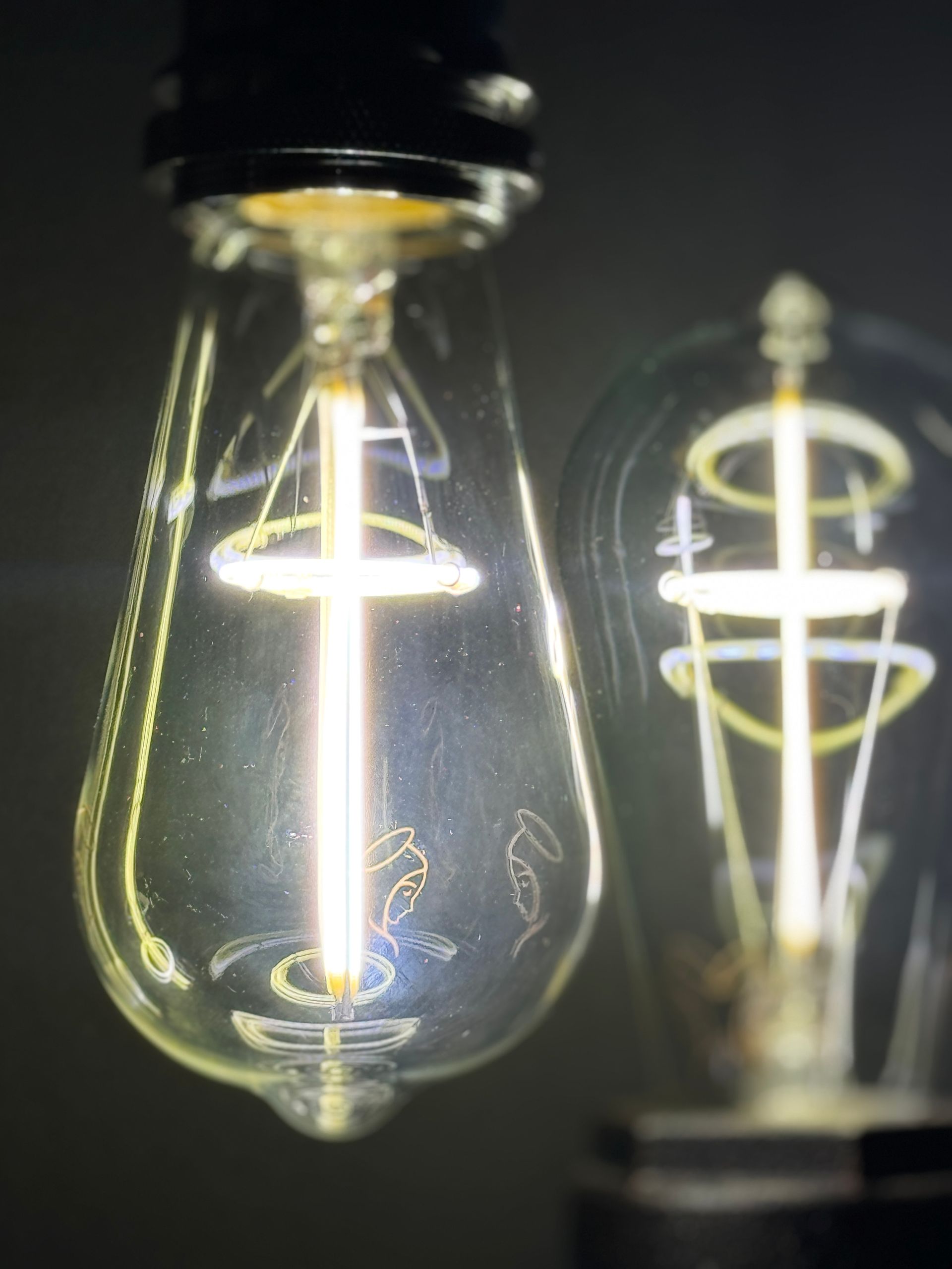 Two illuminated teardrop-shaped light bulbs with a cross-shaped filament.