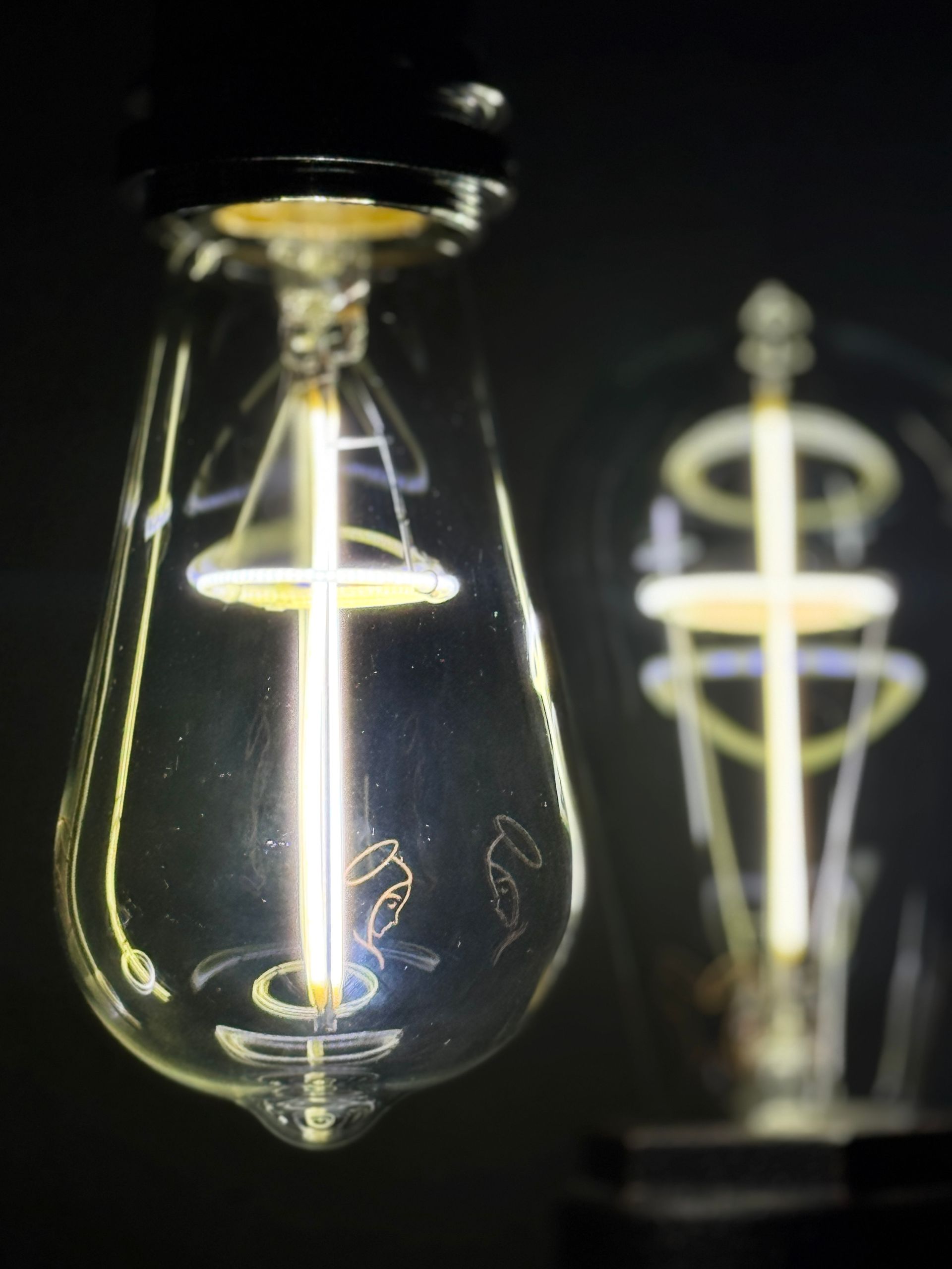 Two lit vintage-style LED light bulbs, one in focus, with a warm glow against a dark background.