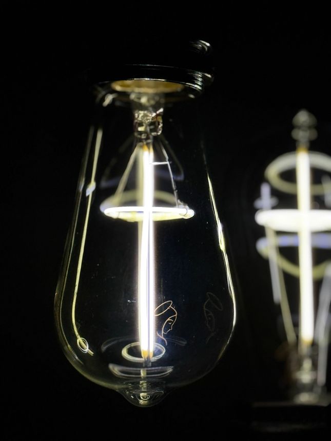 Lit Edison bulb against a black background. Bulb has a long central filament and is partially in focus.