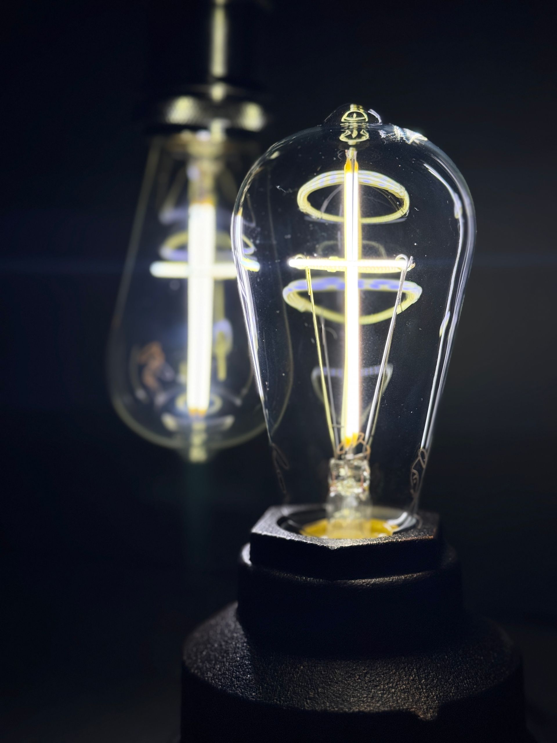 Two Edison-style light bulbs with glowing filaments. One is in focus, resting on a black base.