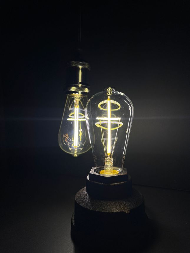 Two Edison-style light bulbs, one hanging, one on a base, glowing brightly against a dark background.