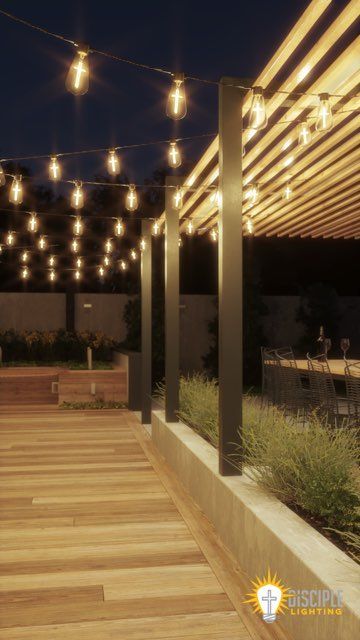 Outdoor patio with string lights, wooden deck, pergola, and dark blue sky at dusk.