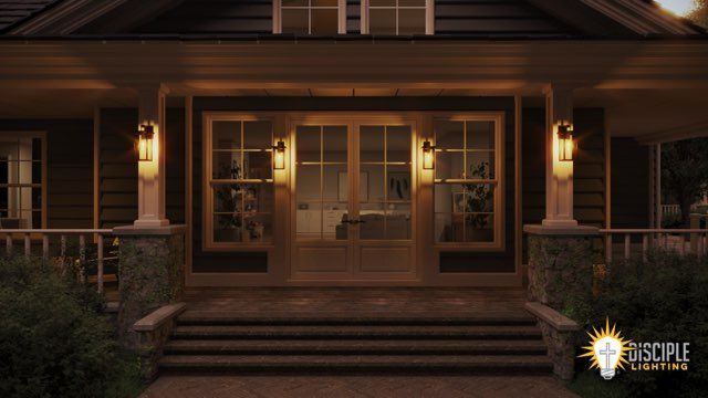 Lit entryway to a house at dusk with glass doors and sidelights, porch and steps.