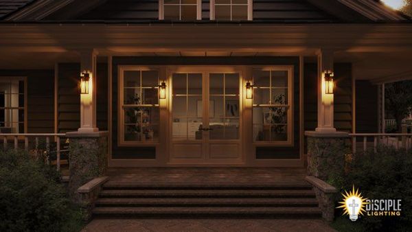 Lit entrance of a house at night, windows reflecting interior light, flanked by sconces.