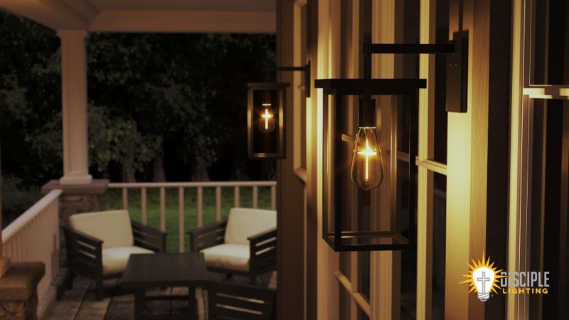 Two outdoor lanterns with lit cross bulbs on a striped wall next to a porch with seating at night.
