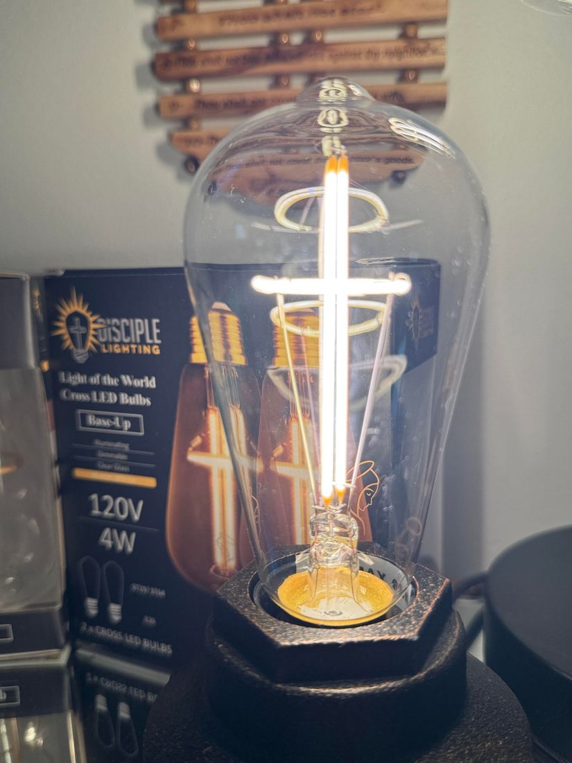 A decorative lightbulb with a cross-shaped filament; box in background, wooden wall decor above.