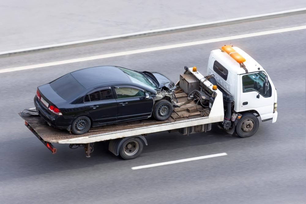 A Tow Truck is Towing a Black Car on a Highway — Bulahdelah Towing In Karuah, NSW