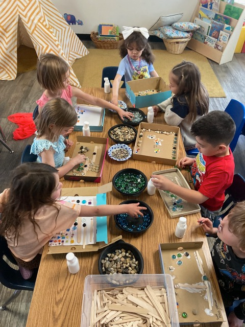 Two children in a classroom gluing colorful paper shapes to blue paper.