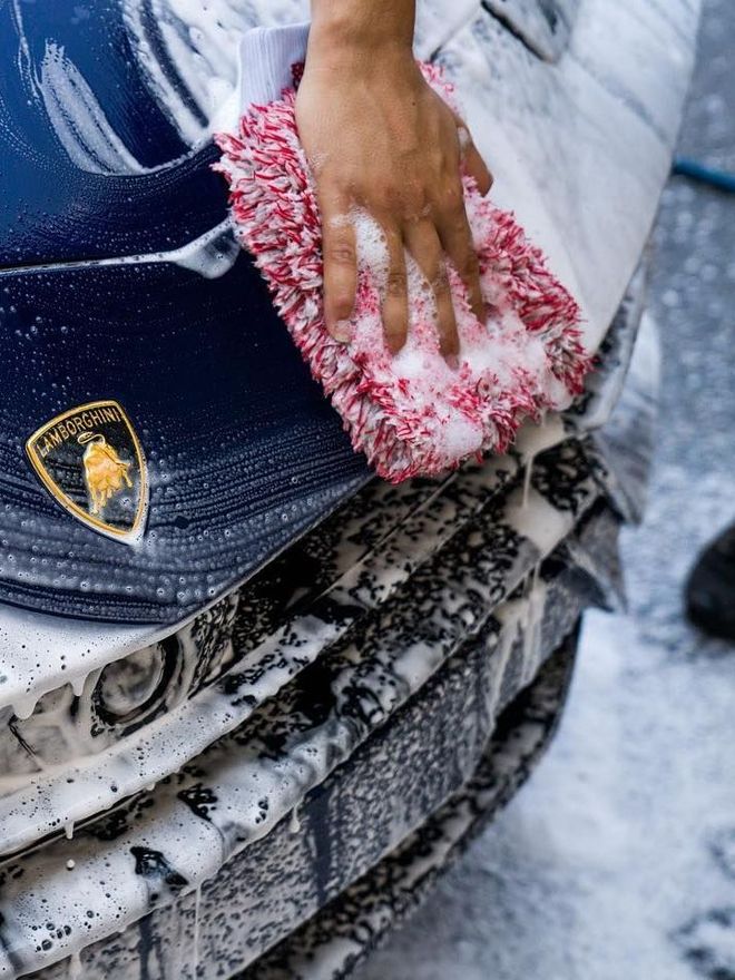 A person is using a blue squeegee to remove plastic from the hood of a car