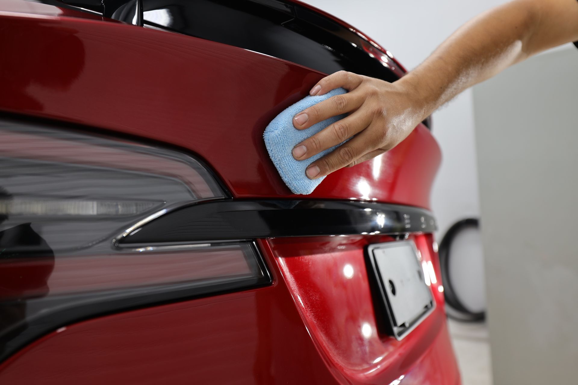 A person is polishing the hood of a blue car.