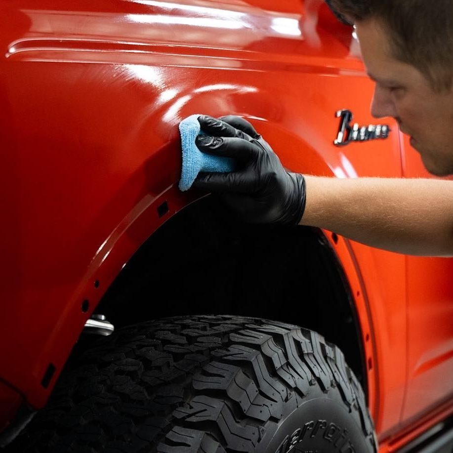 A person wearing black gloves is polishing the hood of a red car.