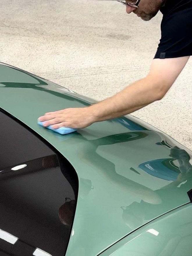 A person is applying a clear film to the hood of a car.