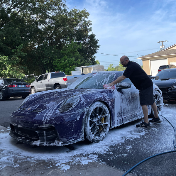 A person is cleaning a blue car with an orange towel