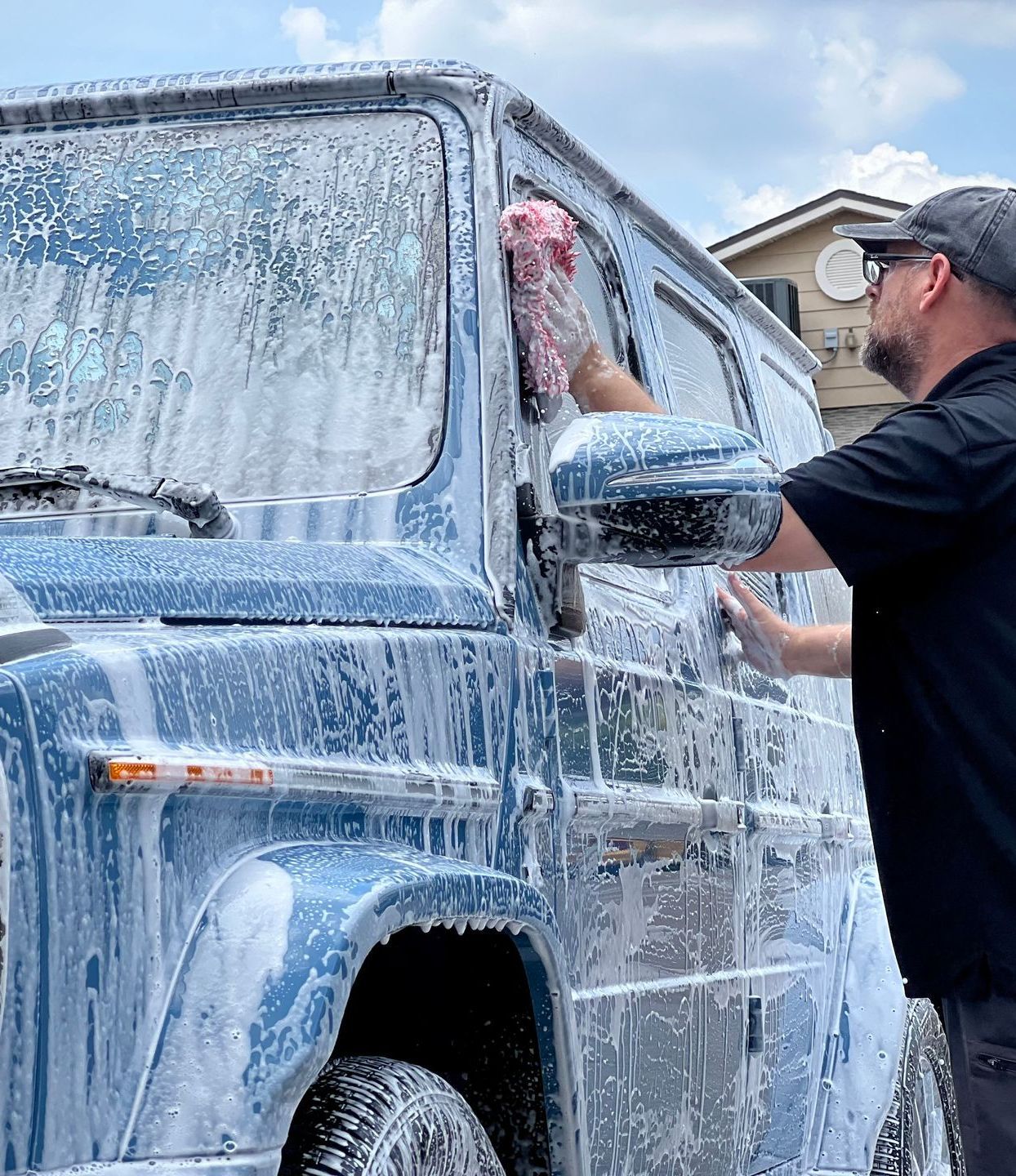 A person is washing a black car with soap and water.