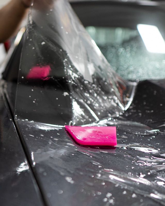 A person is applying a clear film to the hood of a car.