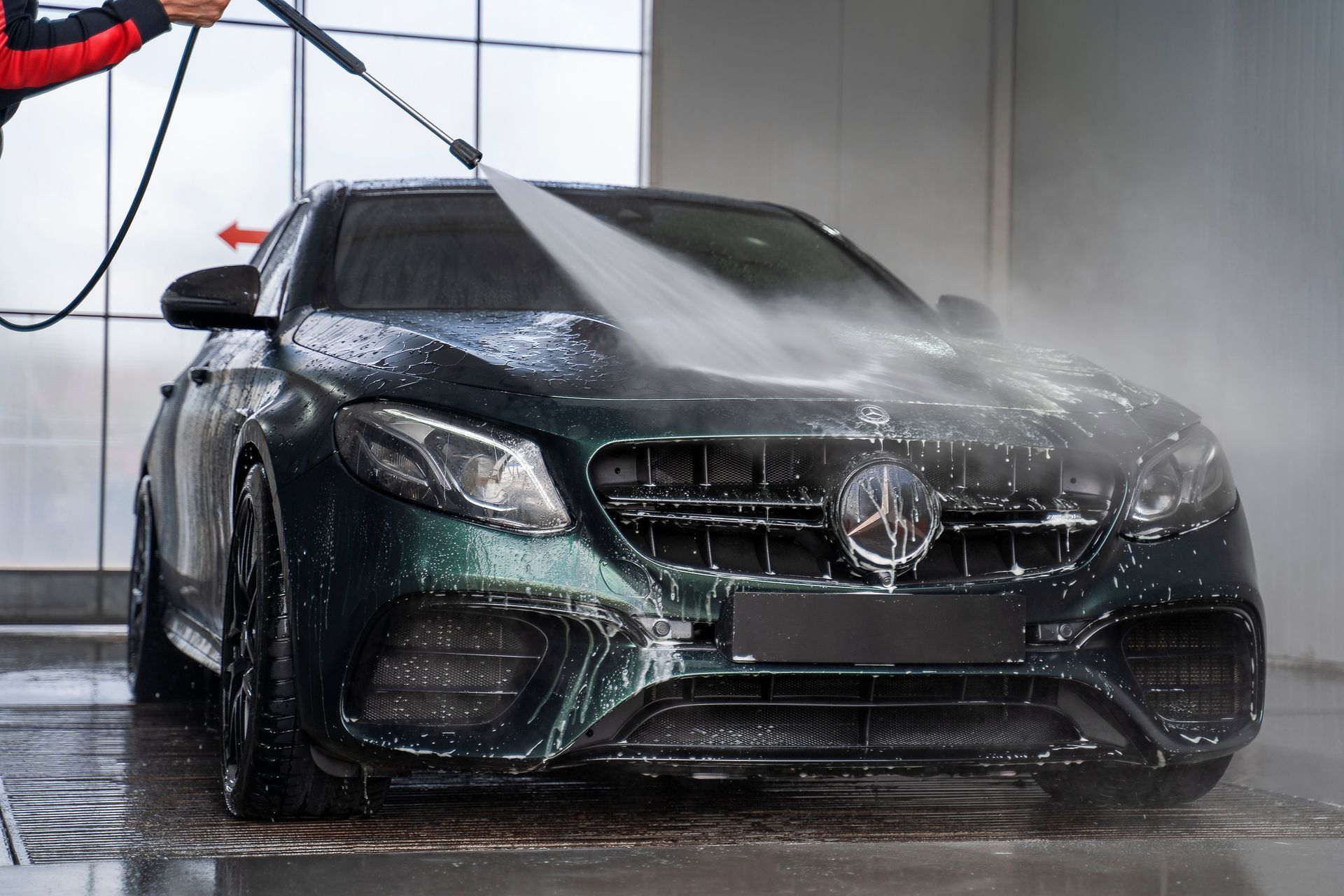 A man is washing a car with a high pressure washer.