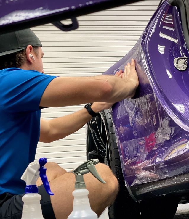 A man is cleaning the wheel of a black car with a sponge.