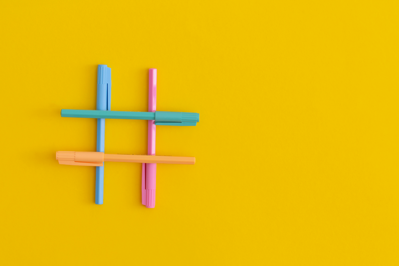 A hashtag symbol made of colorful pens on a yellow background.
