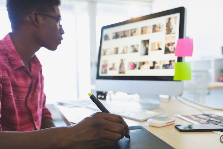 Man using stylus on tablet at computer, looking at screen with various images.