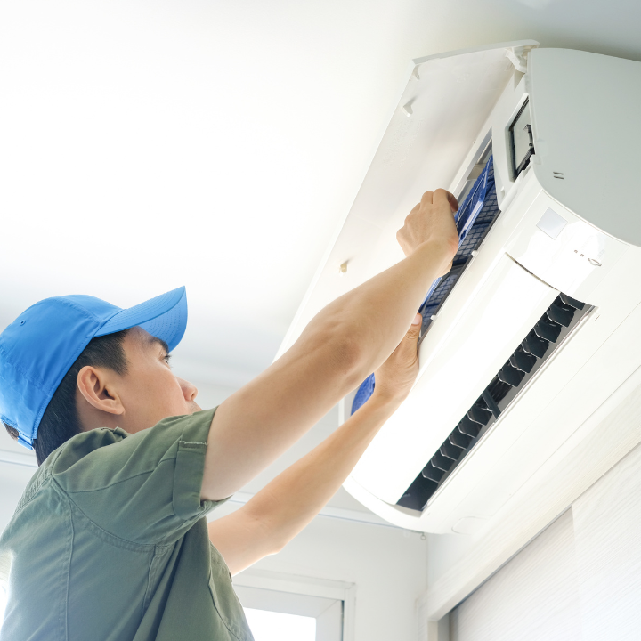 A man wearing a blue hat is working on an air conditioner