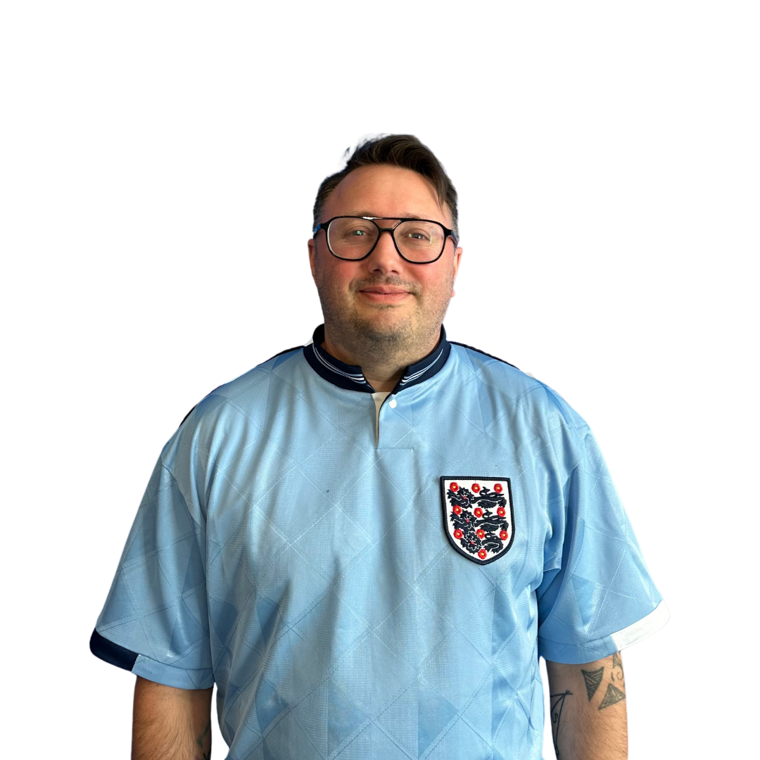 A man wearing glasses and a light blue shirt is standing in front of a white background.