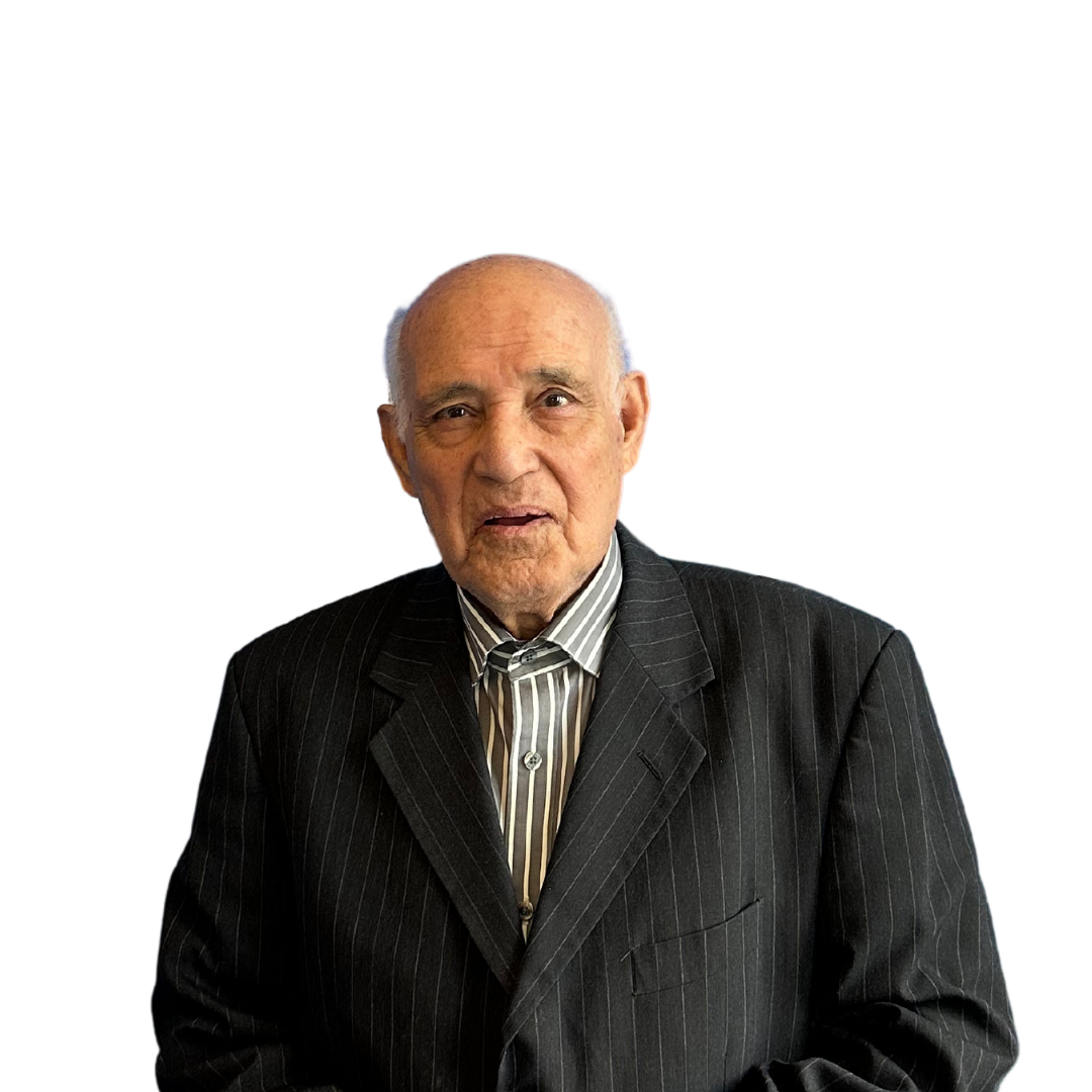 An older man in a suit and striped shirt is standing in front of a white background