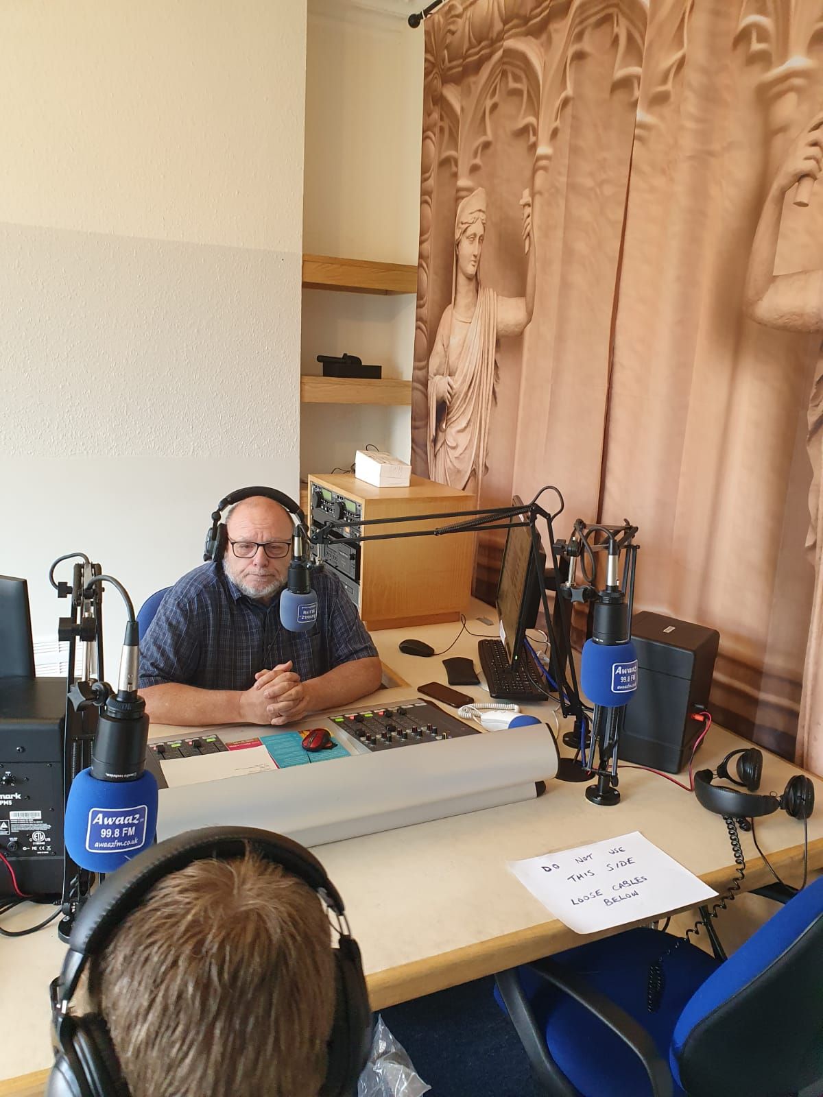 A man wearing headphones is sitting at a desk in front of a microphone.