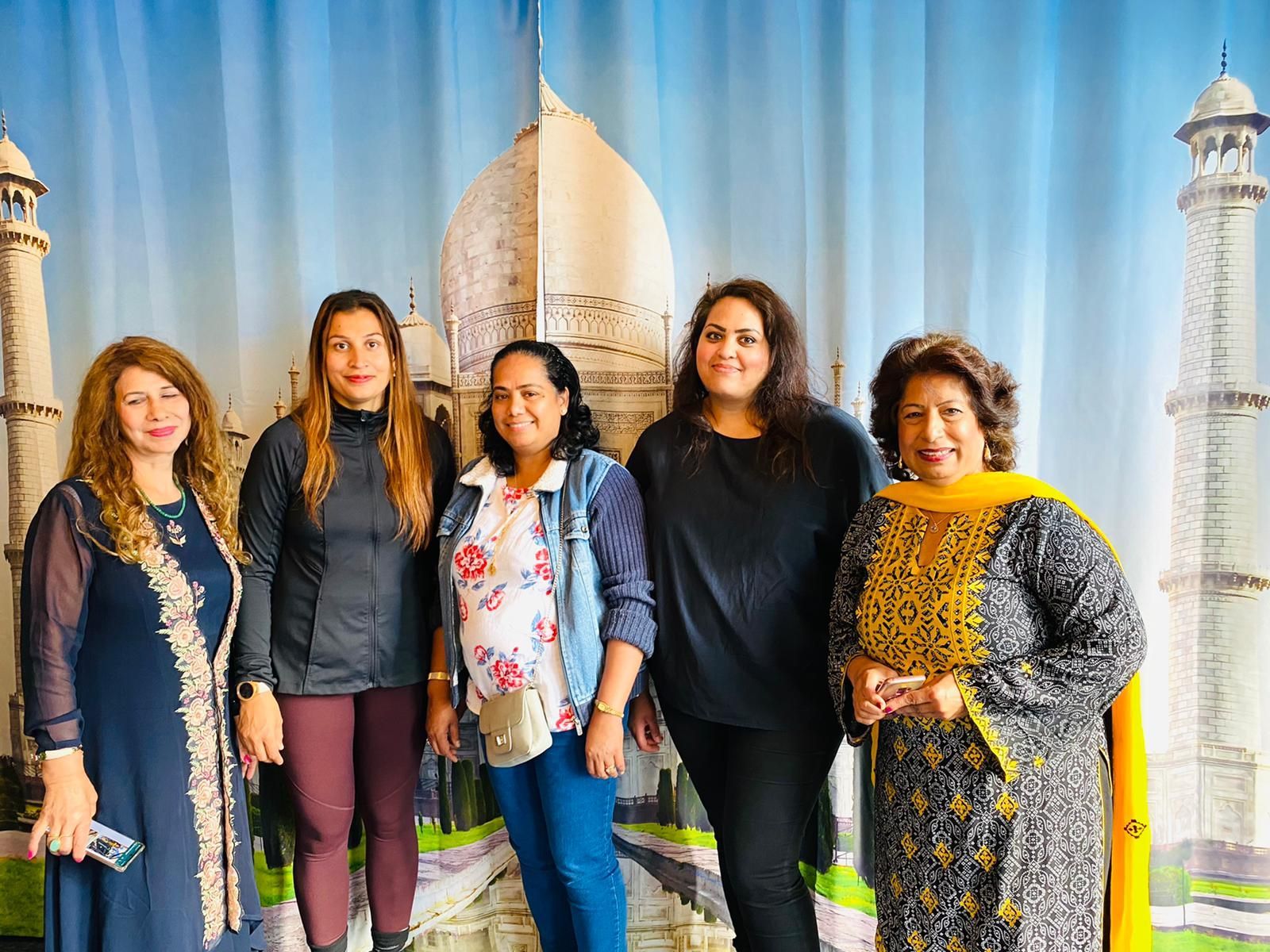 A group of women are posing for a picture in front of a taj mahal backdrop.