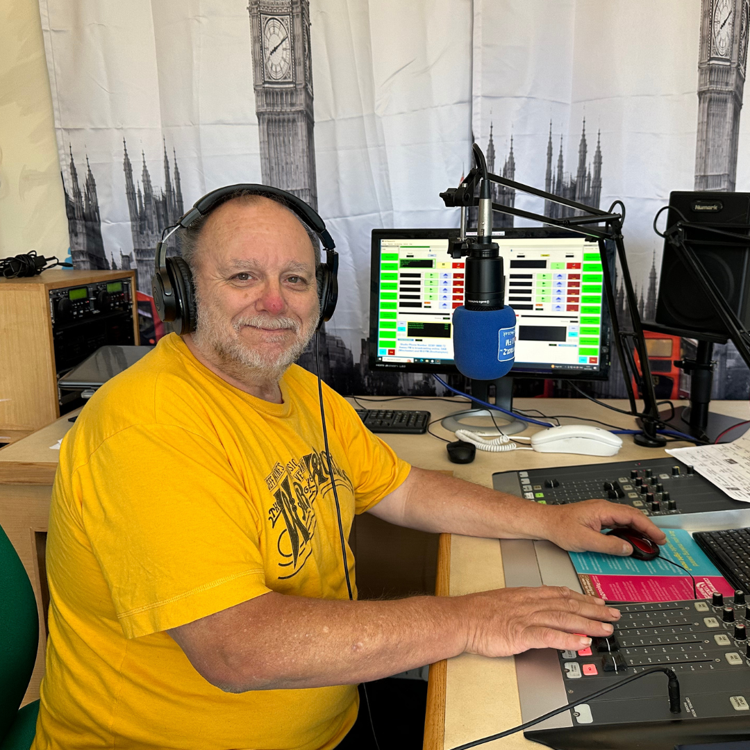 A man wearing headphones is sitting at a desk in front of a microphone.