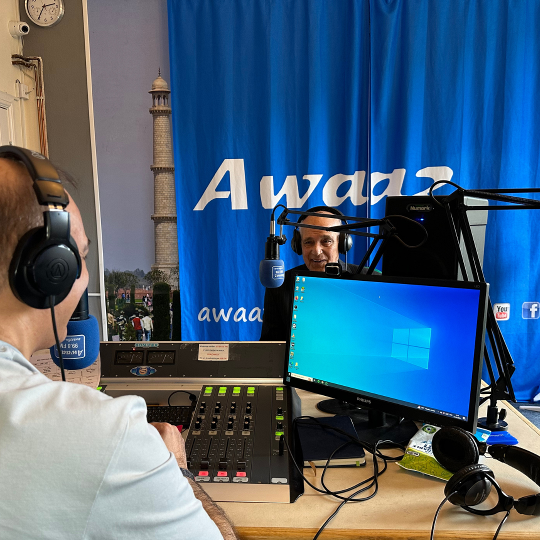 A man wearing headphones sits in front of a blue curtain that says awar