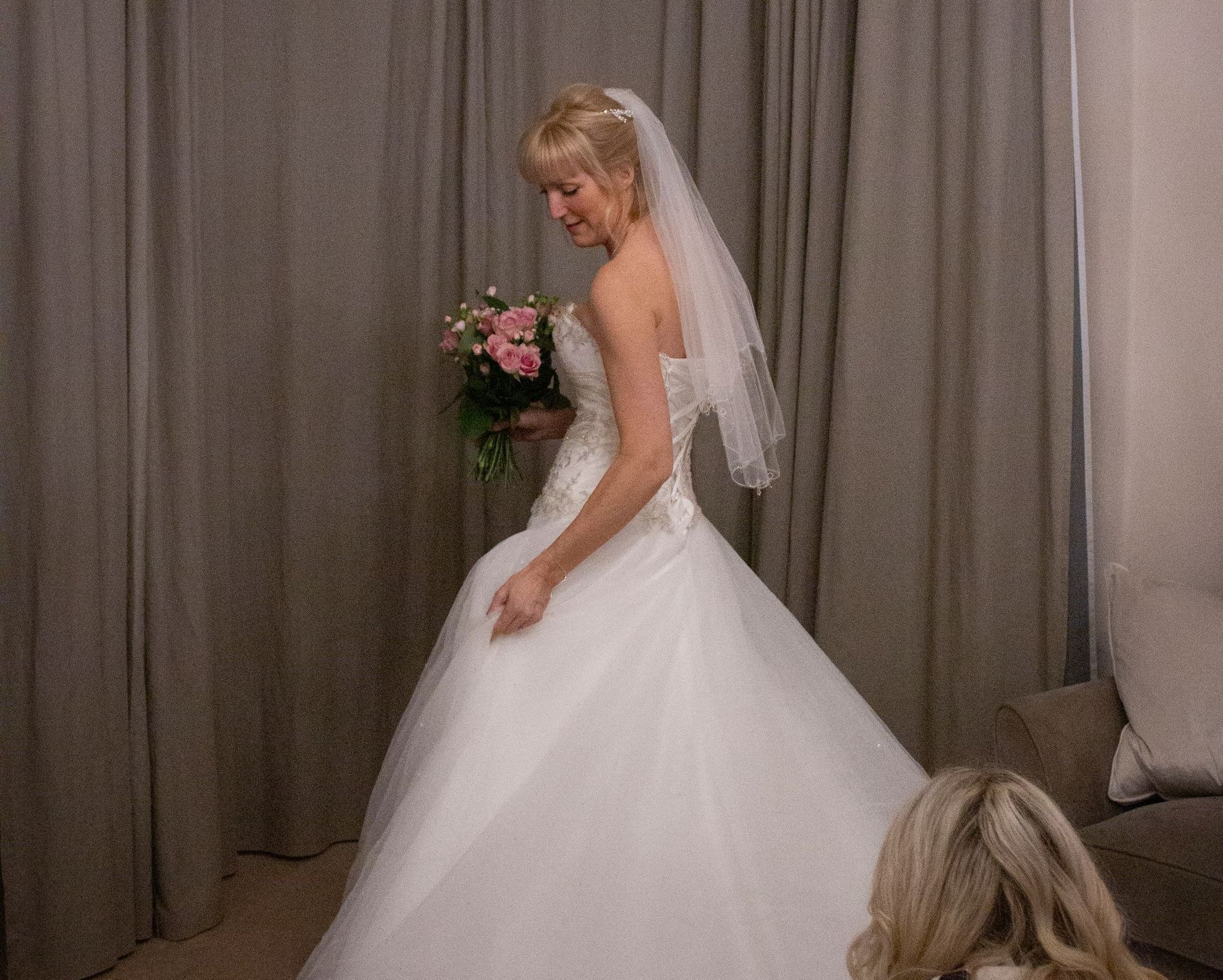a woman in a wedding dress is standing in a room holding a bouquet of flowers .