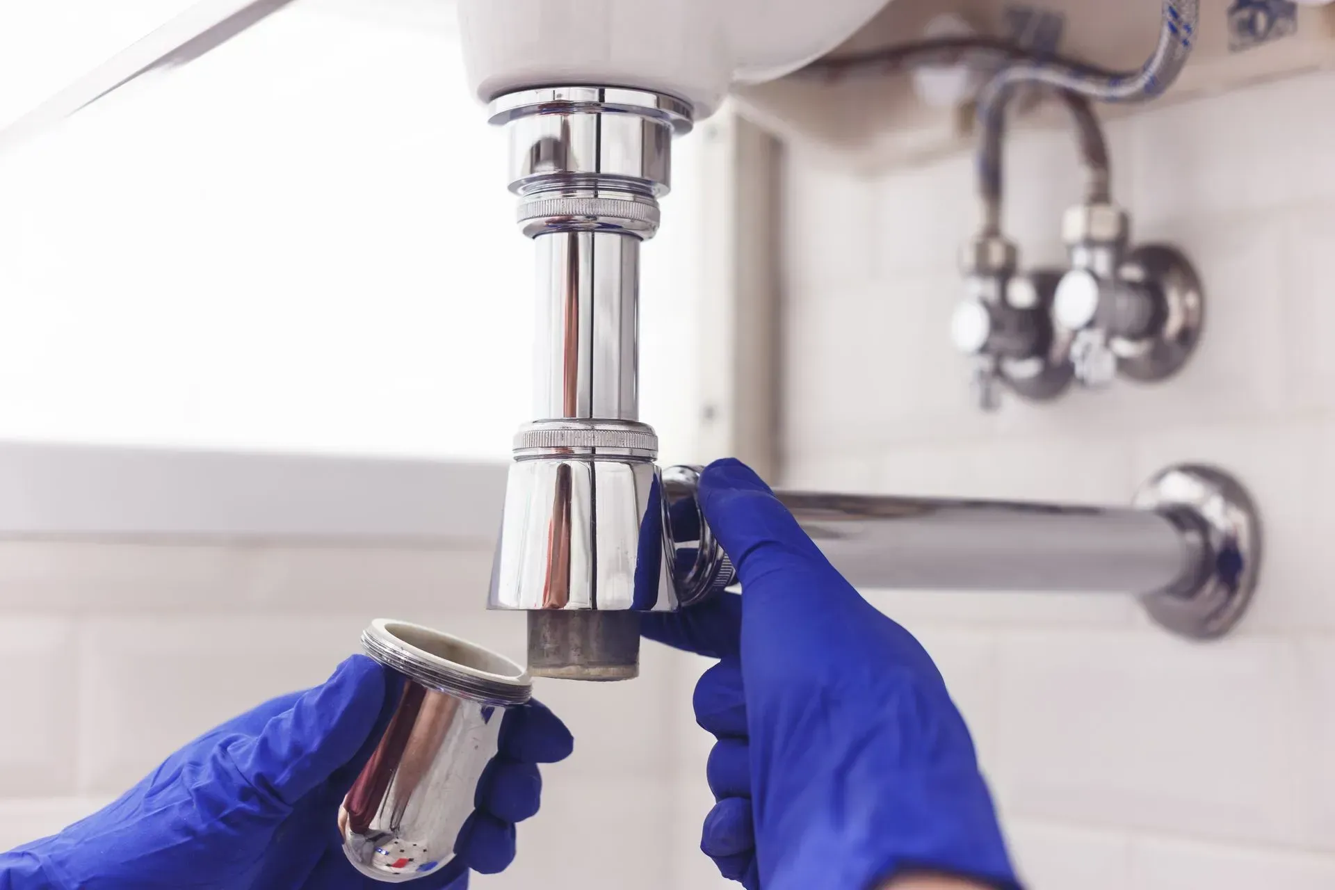 Gloved hands installing a chrome sink drain under a bathroom sink