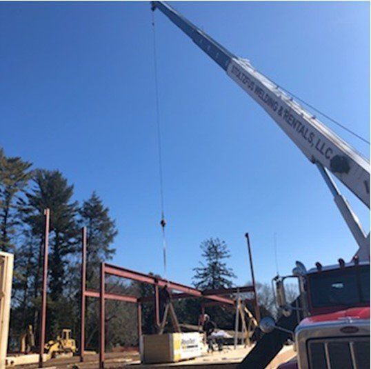 Crane lifting steel beams for a building frame at a construction site on a sunny day.