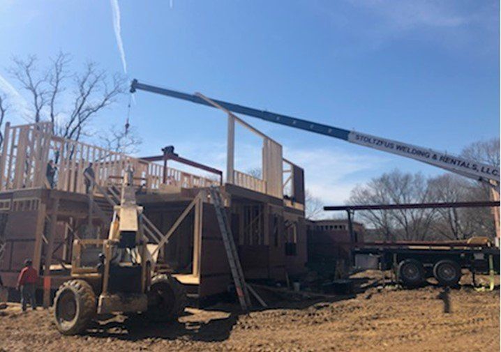 Construction site with crane lifting wall frame. Men working on wooden structure, sunny day.
