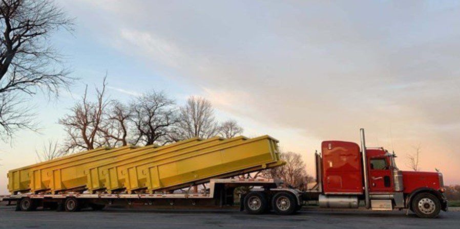 Red semi-truck hauling several large, yellow metal containers on a flatbed trailer against a partly cloudy sky.