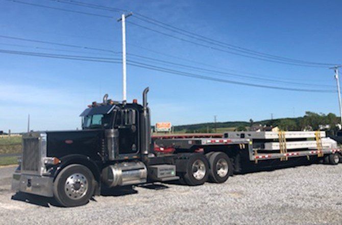Black semi-truck hauling concrete beams on a flatbed trailer on a sunny day.