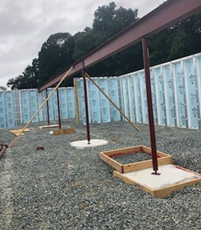 Construction site with red steel beams and supports on concrete pads, against blue and white insulated wall panels.