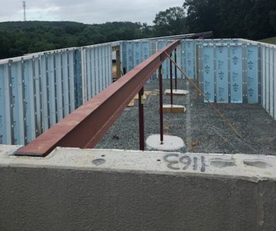 Foundation of a building with blue insulated walls and a brown steel beam supported by vertical poles.