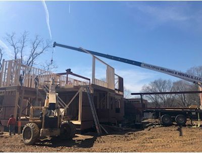 Construction site: crane lifting wooden wall panel. Workers building a structure outdoors on a sunny day.