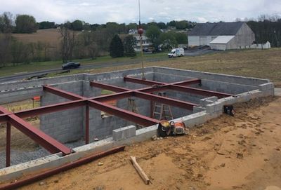 Construction site with red steel beams being placed on gray concrete block foundation. Crane visible.