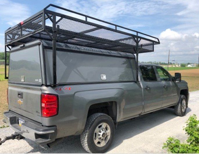 Gray pickup truck with a black utility topper and roof rack parked on a road.