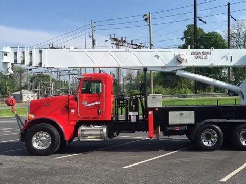 Red and black crane truck parked on asphalt; utility lines in background.