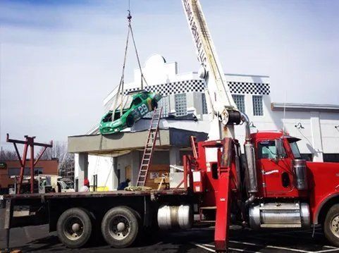 Red crane lifting a green car off a building's roof with checkered trim.