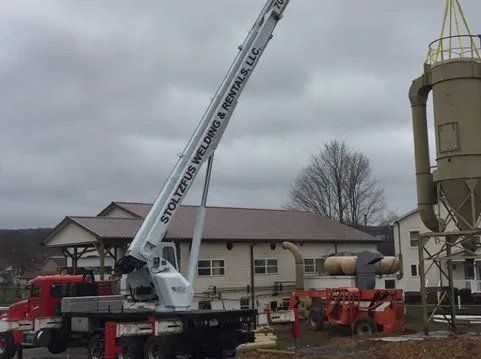 Crane truck lifting a large industrial silo; cloudy outdoor setting.
