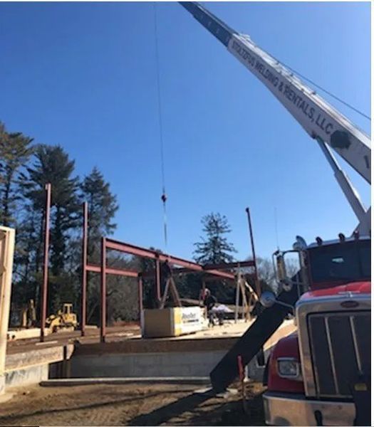 Crane lifting steel beams at a construction site on a sunny day.