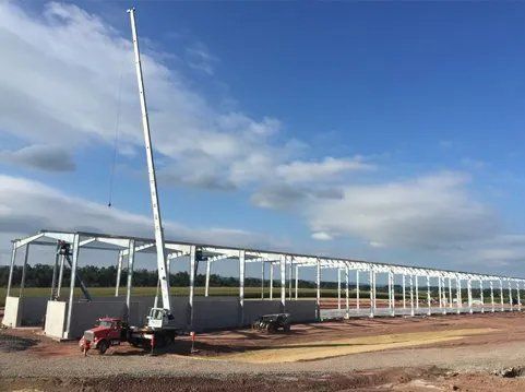 Construction site with tall crane erecting steel frame of long building under a blue sky.
